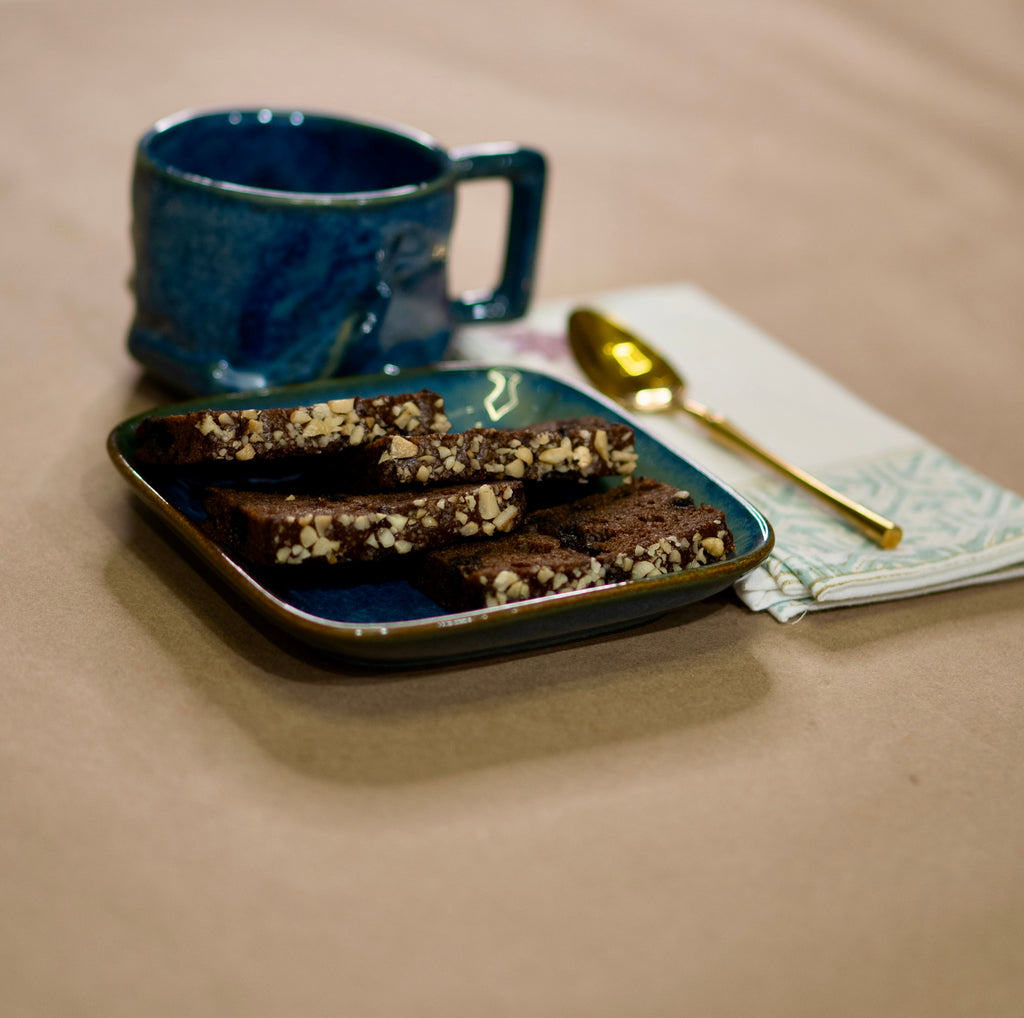 Blue mug with a plate of brownies and a gold spoon on a beige surface