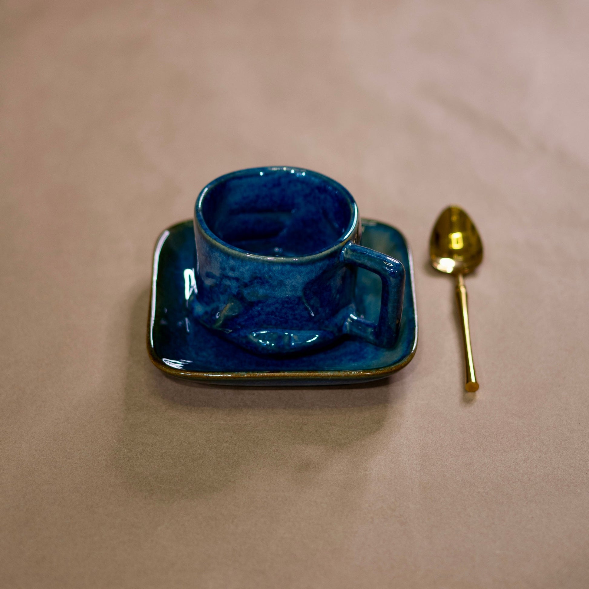 Blue ceramic cup and saucer with a gold spoon on a beige surface