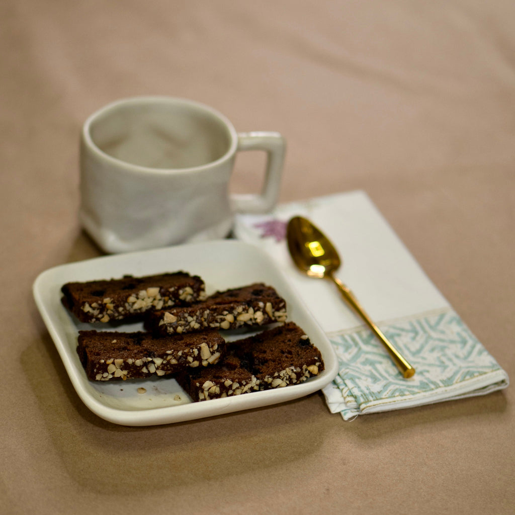 matte white Plate of brownies with a matte white yunomi mug and gold spoon on a beige surface
